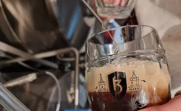 Beer glass filling with dark beer in brewery.