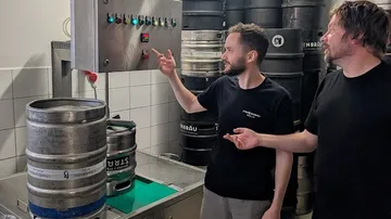Zwei Männer bedienen Brauereiausrüstung in einer Brauerei.