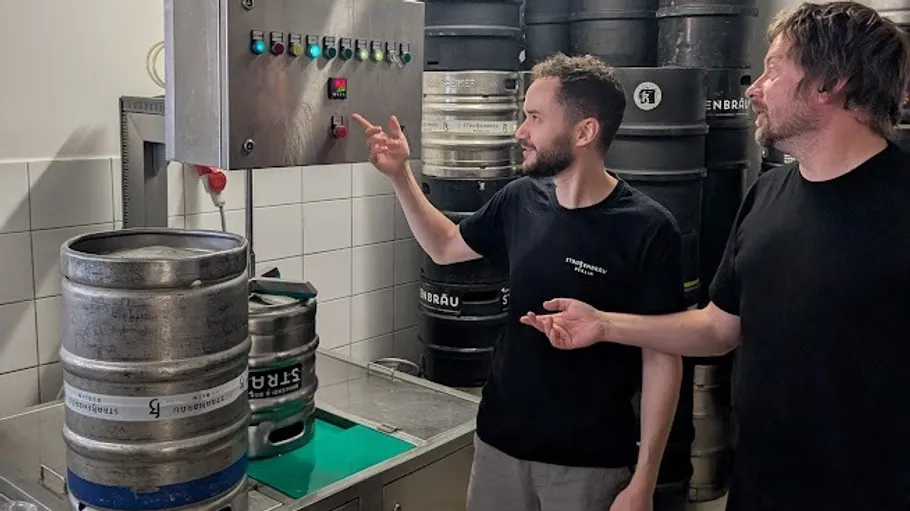 Two men operate brewing equipment in a brewery.