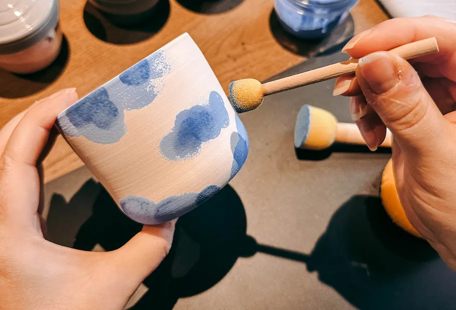 Person bemalt Keramikbecher mit blauem Schwamm.