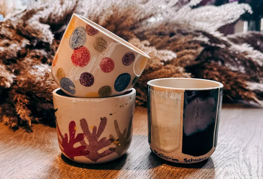 Three decorated mugs on a wooden table.
