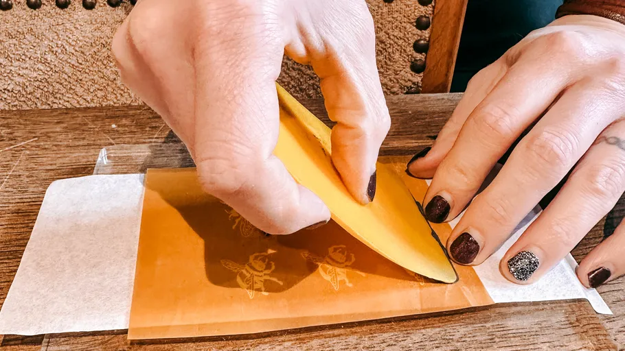 Hands applying wax with a scraper on paper.