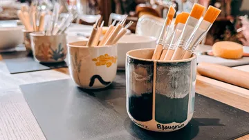 Paintbrushes in decorative mugs on table.