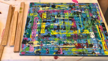 Abstract painting with wooden sticks nearby.