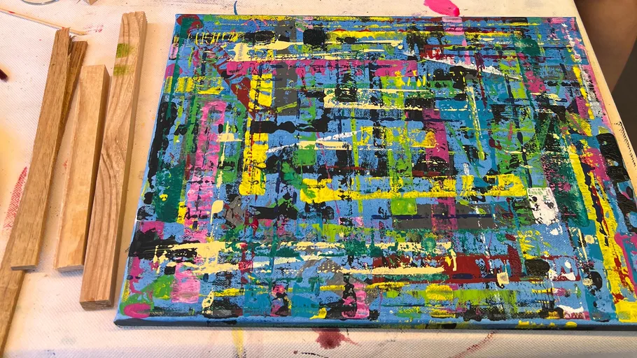 Abstract painting with wooden sticks nearby.
