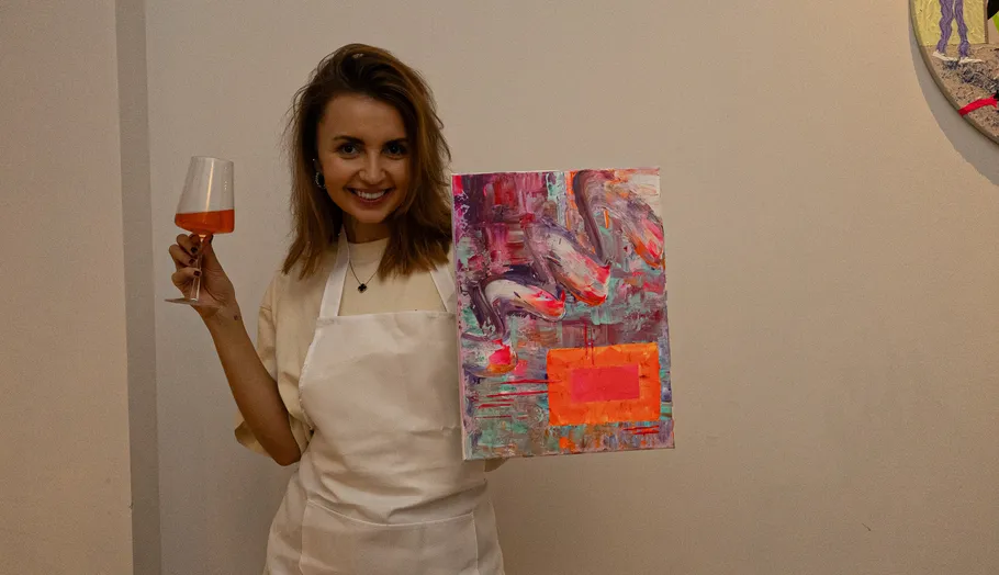 Woman smiles holding wine glass and colorful painting.