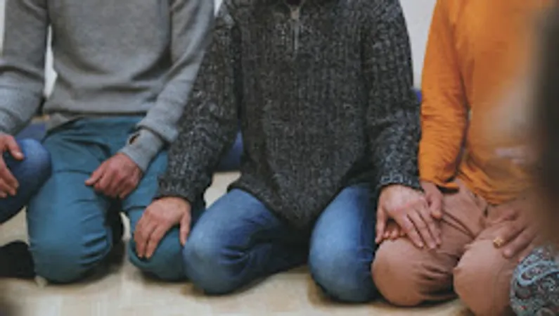People sitting crossed-legged indoors, holding hands.