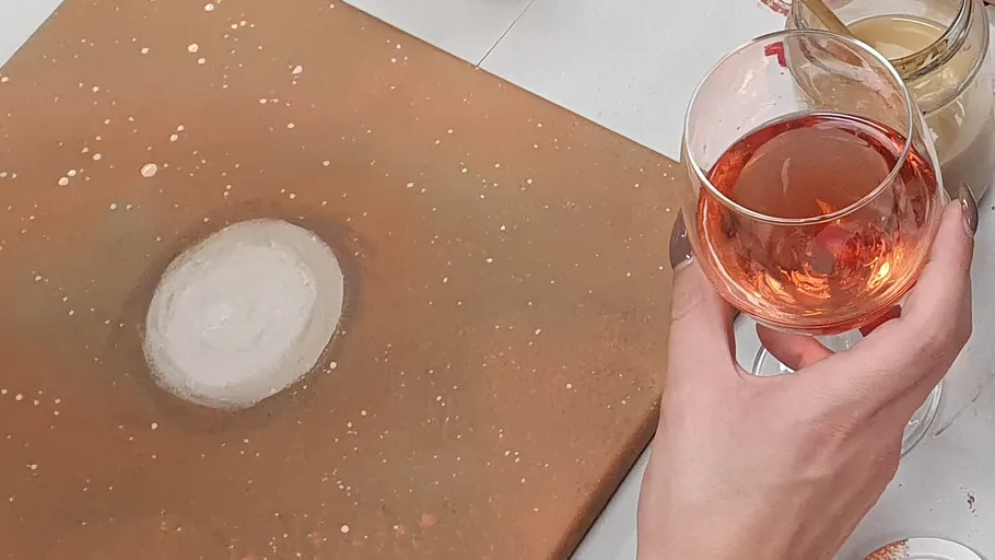 Hand hält Wein neben abstraktem Gemälde.