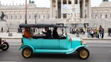 Vintage car driving in front of historic building.