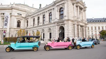 Vintage cars driving past historic building.