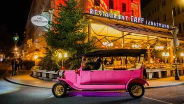 Pink vintage car in front of festive restaurant.