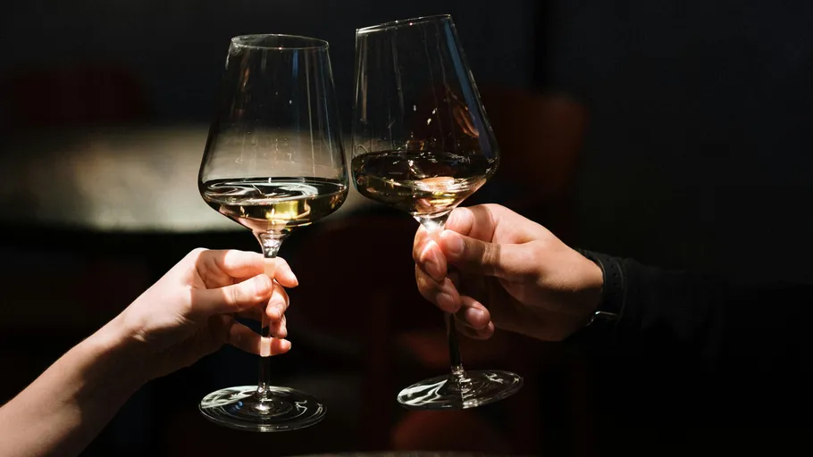 Two hands clinking wine glasses, dimly lit.