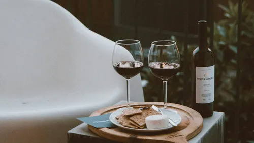 Wine, glasses, cheese, crackers on outdoor table.