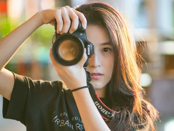 Junge Frau fotografiert mit Kamera in sonniger Umgebung.