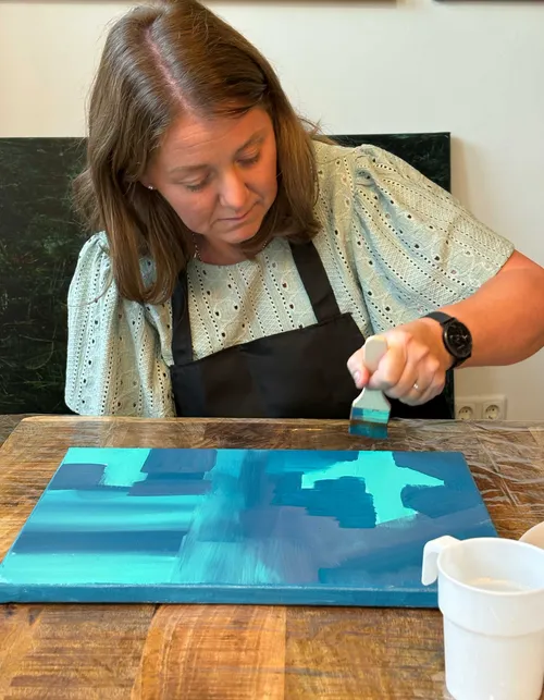 Frau malt auf Leinwand an Holztisch.