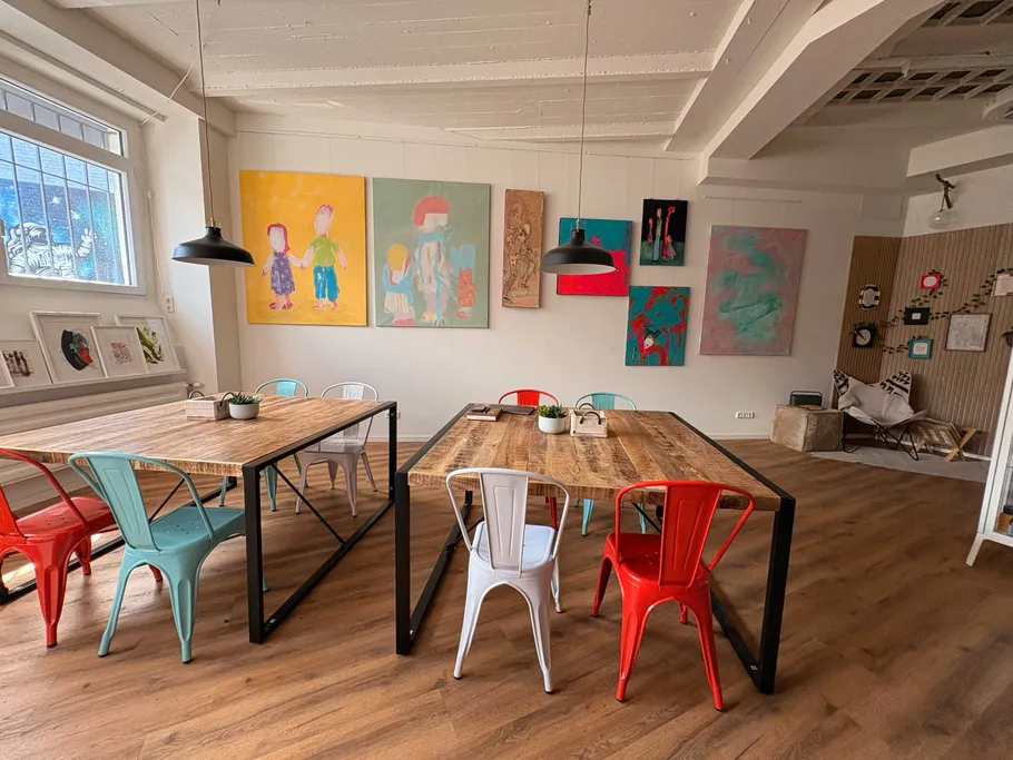 Künstlerischer Arbeitsplatz mit bunten Stühlen und Gemälden.