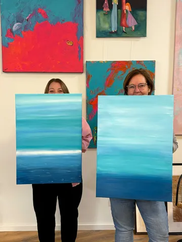 Zwei Personen halten Meerbilder in Kunstgalerie.