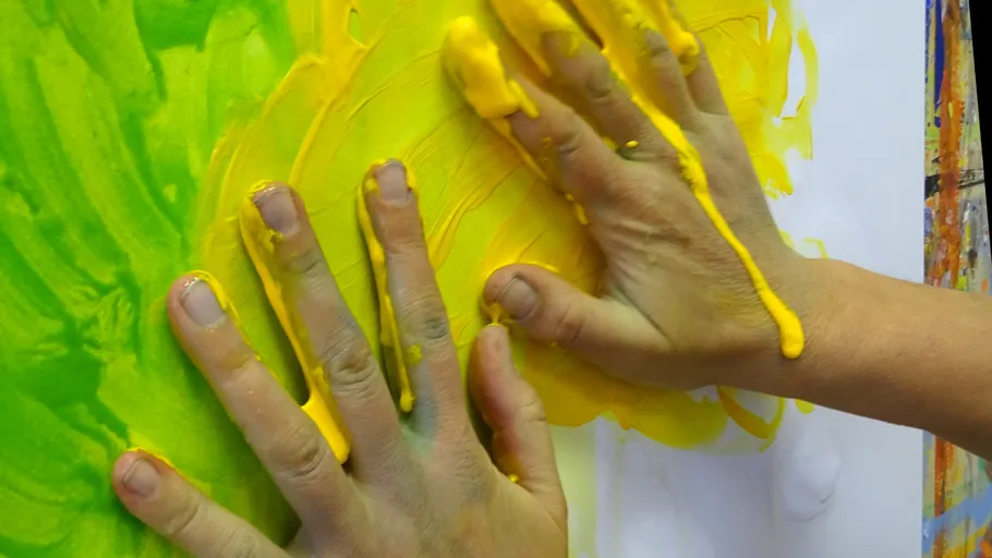 Hands painting yellow and green on paper.