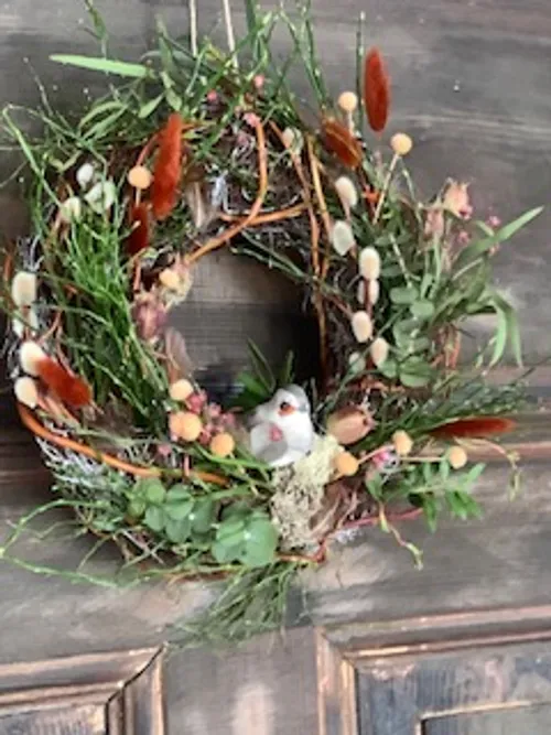 Blumenkranz mit kleinem Vogel an Tür.