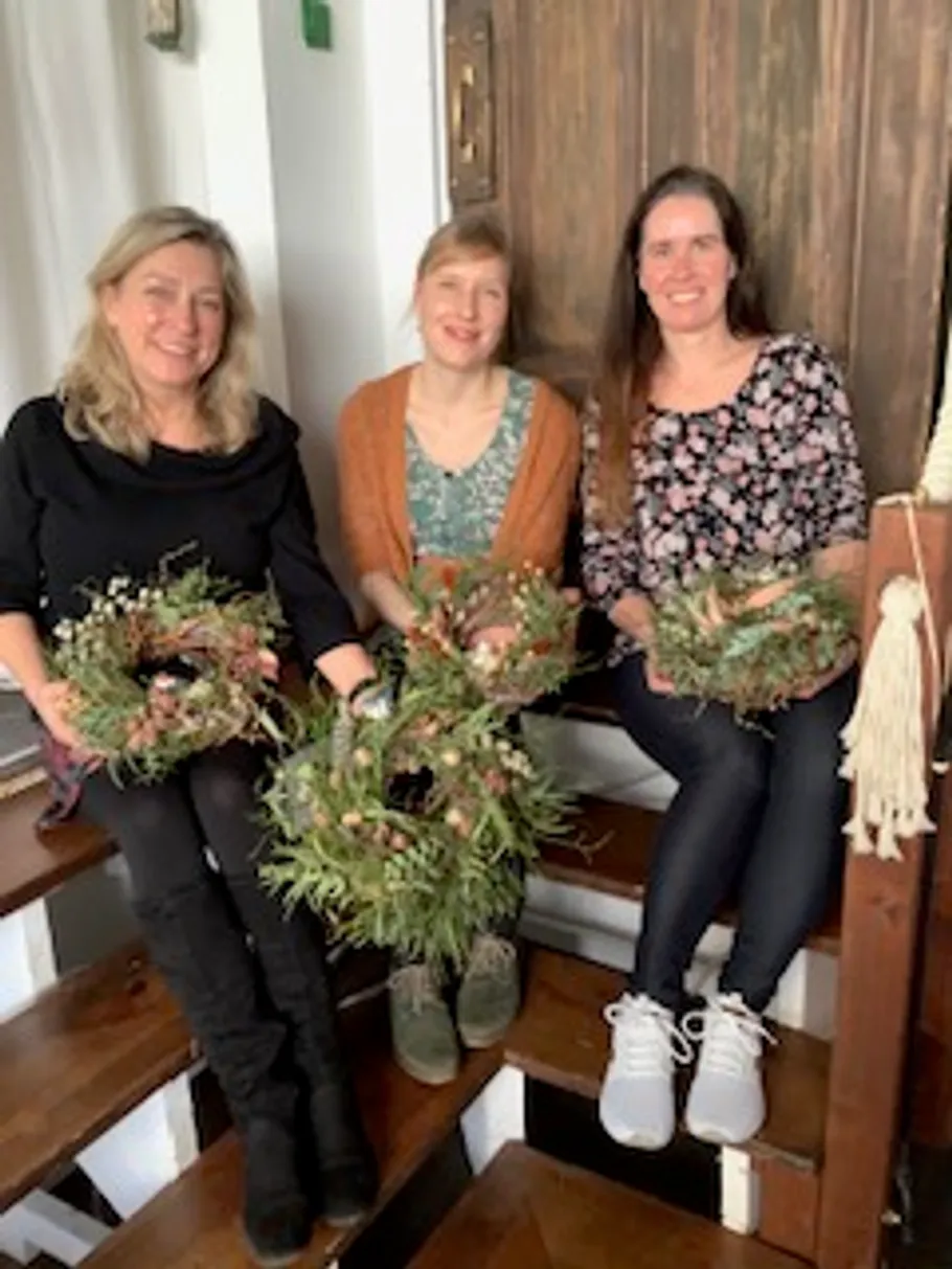 Drei Frauen sitzen drinnen mit dekorativen Kränzen.