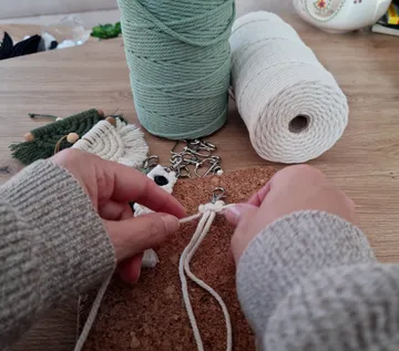 Hands knotting rope on a cork surface.