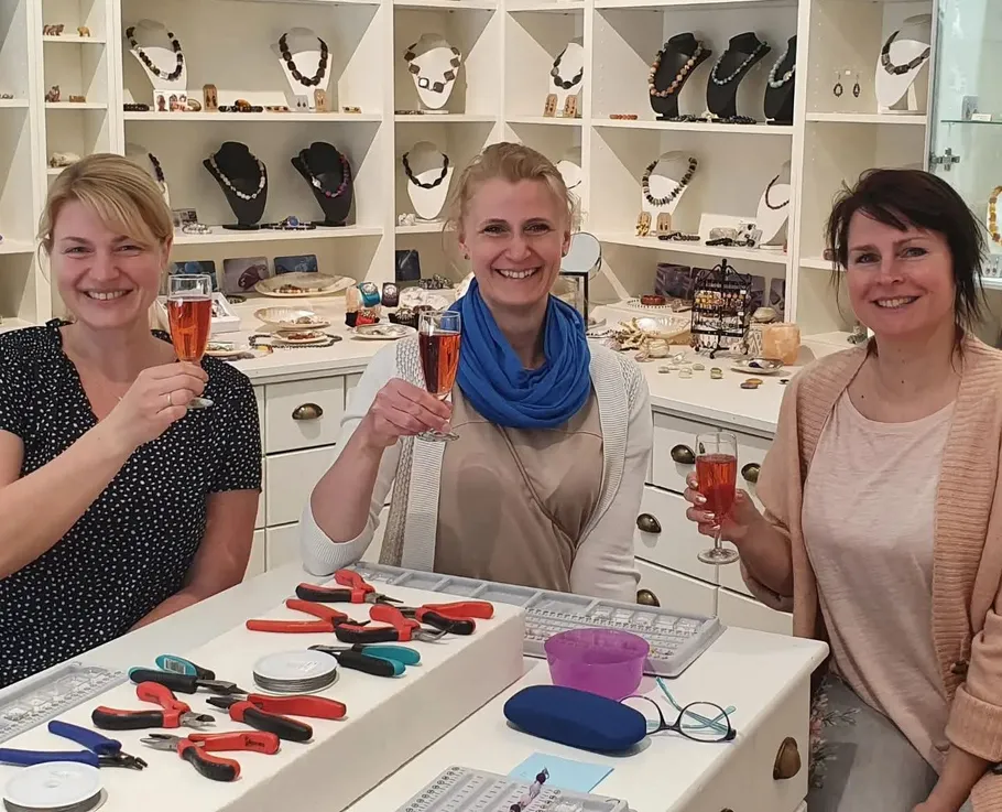 Three women smiling, holding glasses, in a jewelry shop.