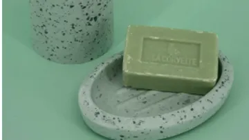 Grüne Seife auf gesprenkelter Schale, zylindrischer Behälter.