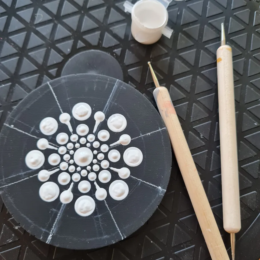 Bemaltes Punktmandala mit Werkzeugen auf Matte.