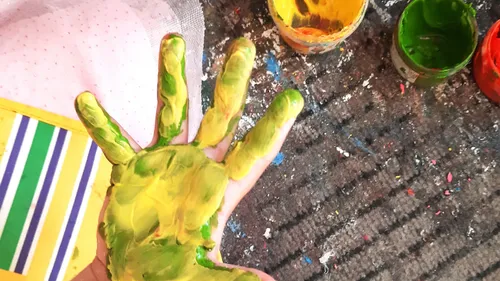 Kinderhand mit Farbe bedeckt, neben Farbtöpfen.
