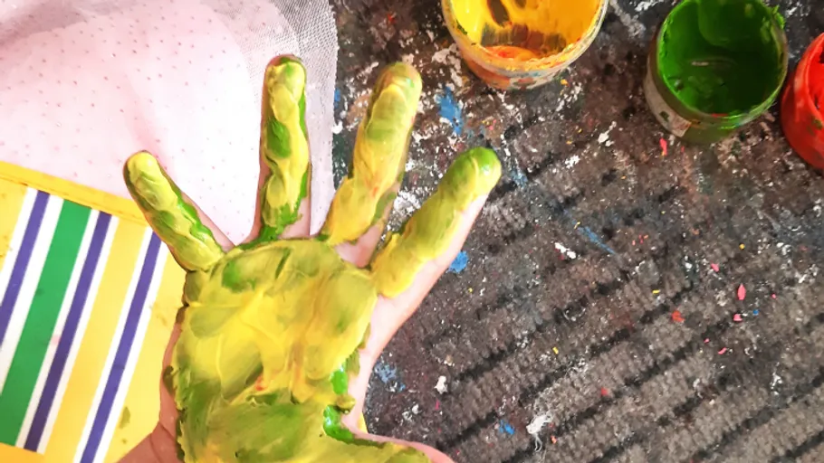 Child's hand covered in paint, beside paint pots.