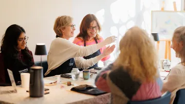 Gruppe von Frauen lächeln um einen Tisch.