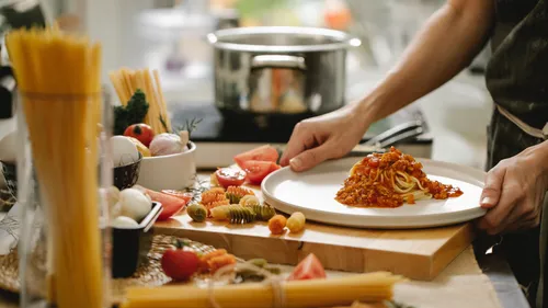 Person serving spaghetti with tomato sauce kitchen.
