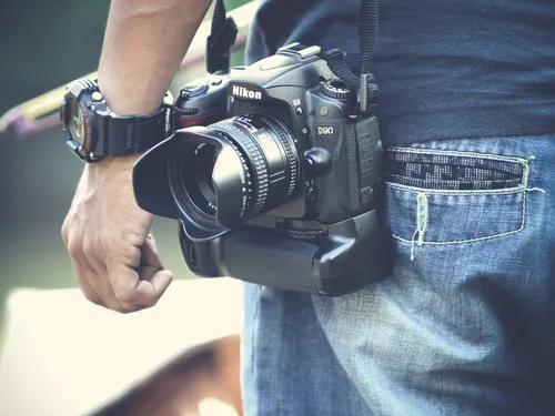 Camera hangs on belt, person holds it with their hand.