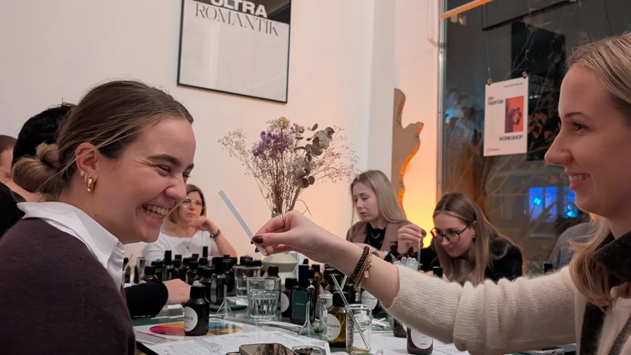Woman smelling scent strip, smiling in workshop.
