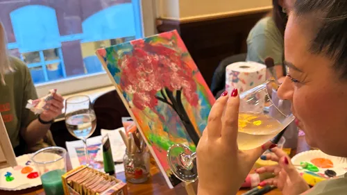 Woman painting and drinking wine indoors.