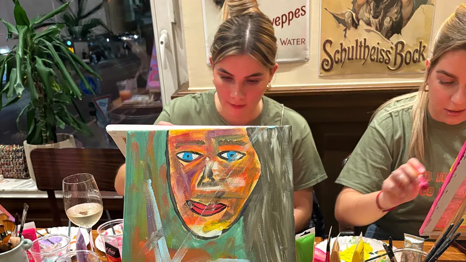Two women painting colorful canvas portraits indoors.