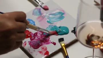 Hand malt auf Palette neben Weinglas.