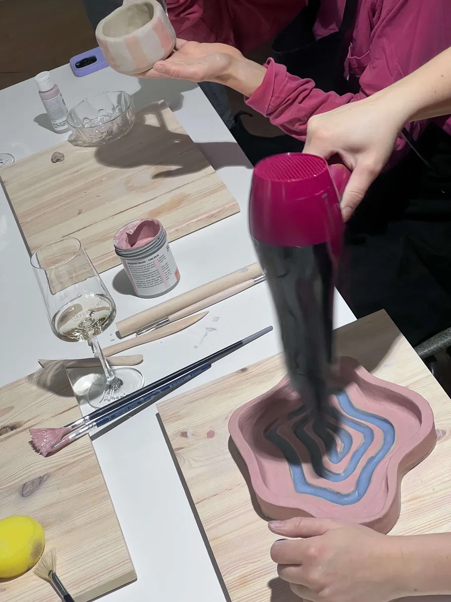 Hands decorating pottery with hairdryer and tools.