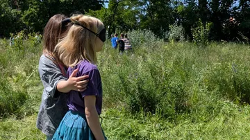 Two people, one blindfolded, walking in a field.