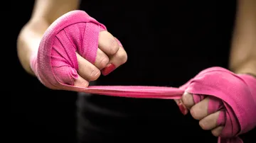 Hände wickeln pinke Boxbandagen, dunkler Hintergrund.