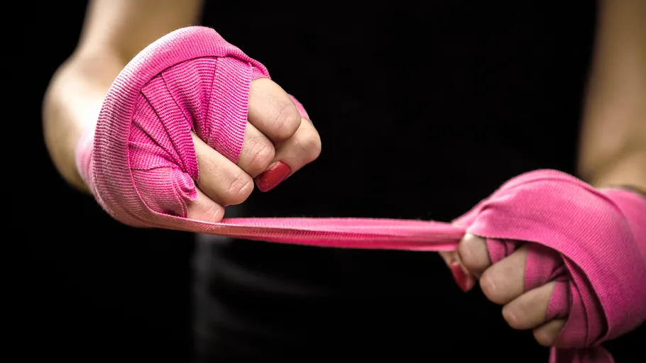 Hands wrapping pink boxing bandages, dark background.