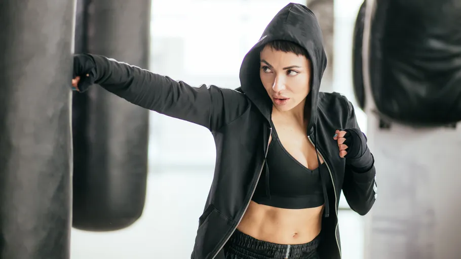 Woman in black hoodie punching boxing bag.