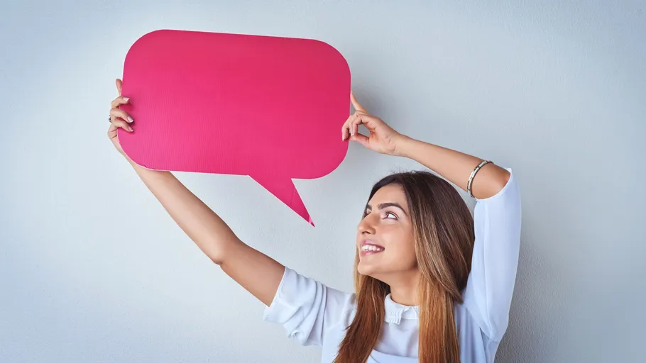 Woman holding pink speech bubble against wall.