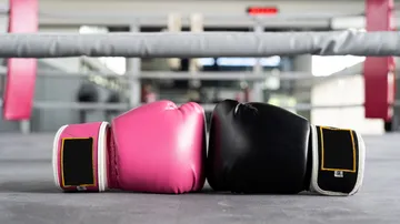 Pink and black boxing gloves in a ring.