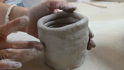 Hands shaping clay on smooth surface.