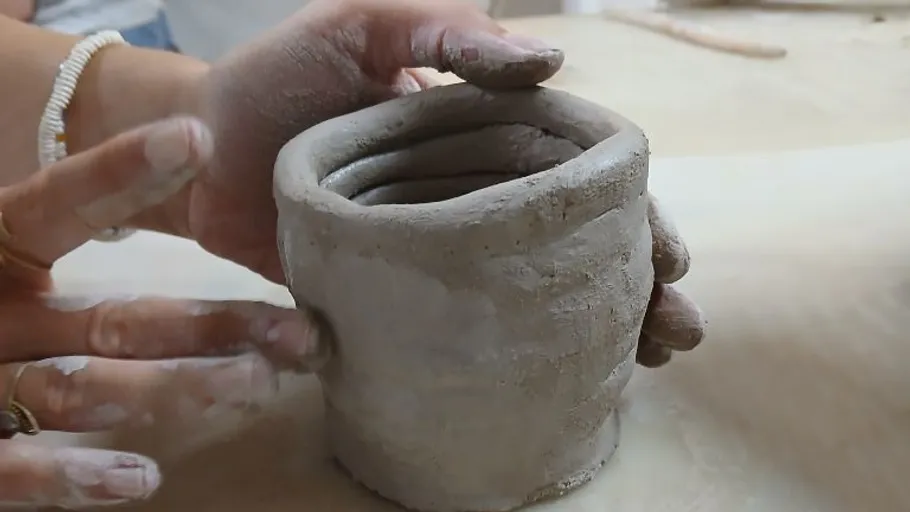 Hands shaping clay on smooth surface.