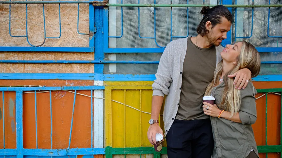 Couple with coffee cups embracing by colorful wall.