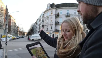 Two people using tablet on city street.