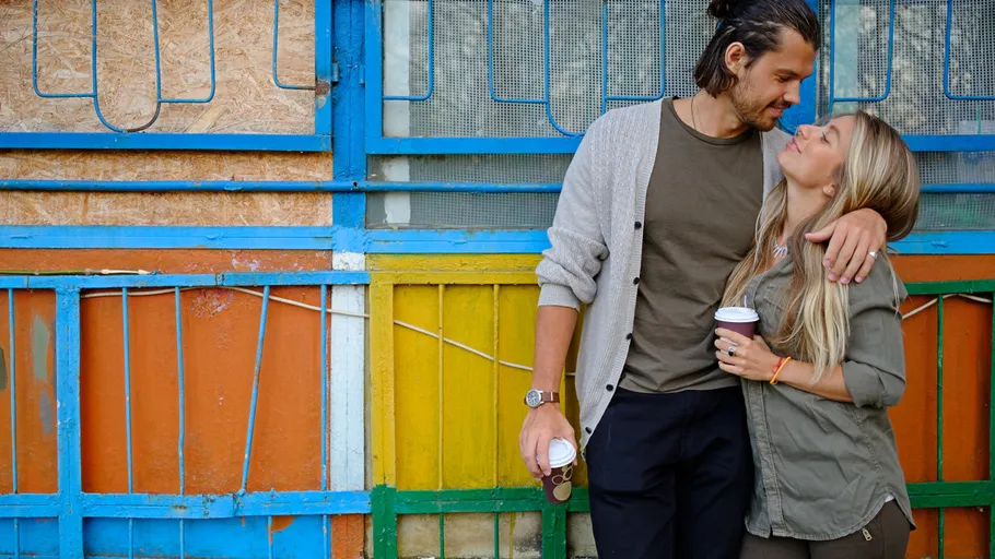 Couple holding coffee in colorful urban setting.