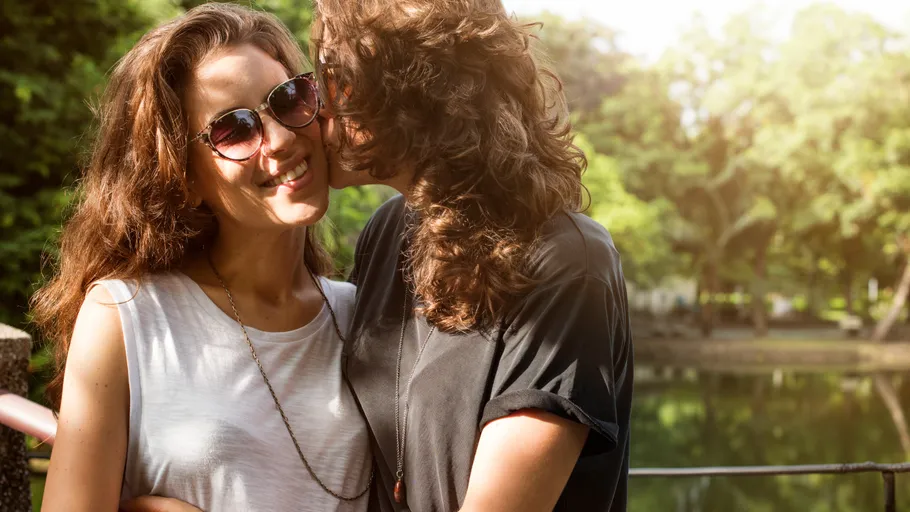 Two people embrace near a sunlit pond.